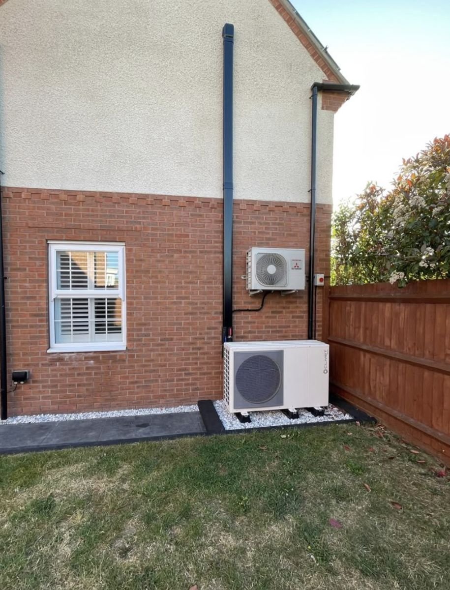 Heat pump outdoor unit on a gravel strip at the side of a house