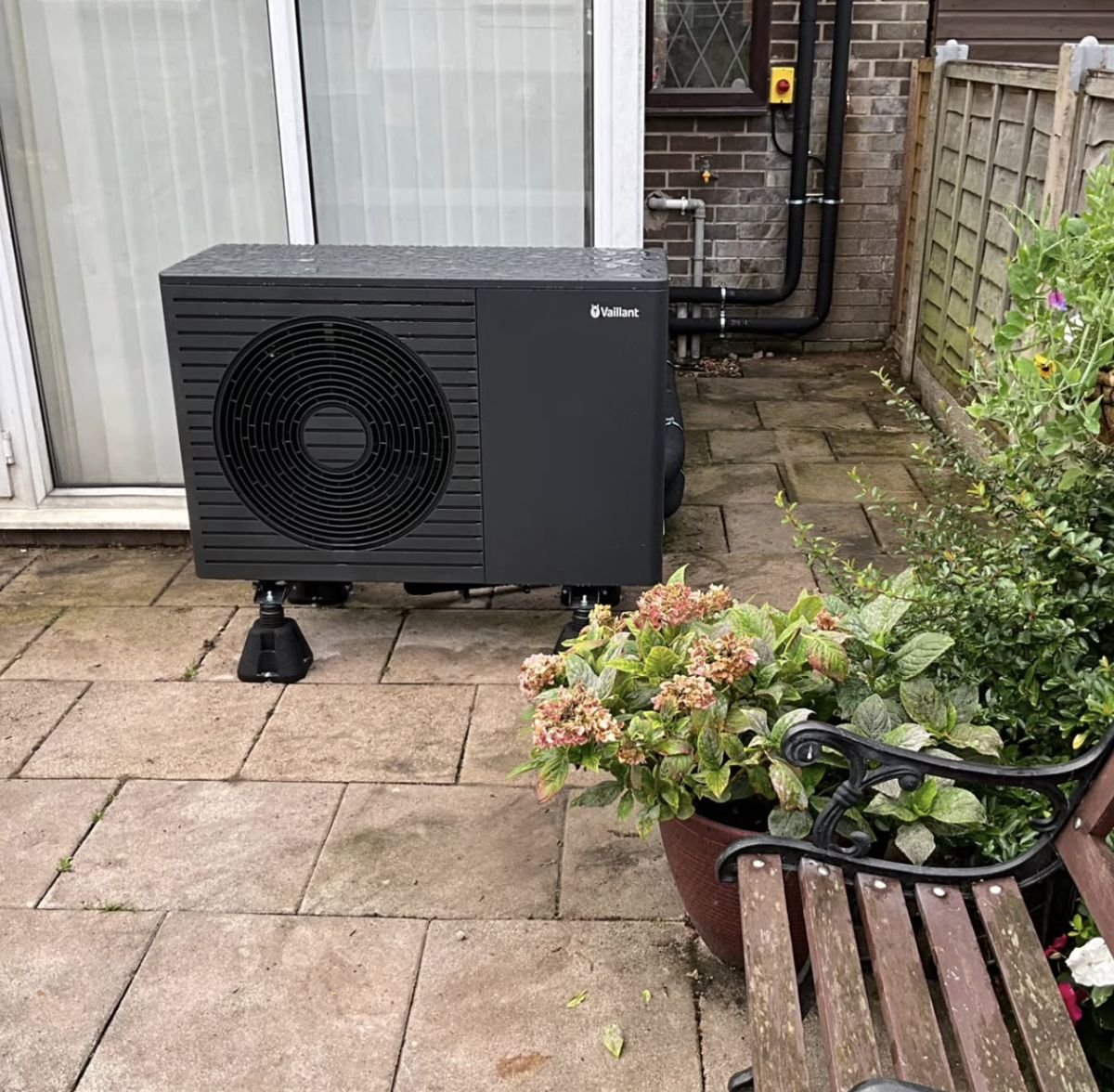 Black Vaillant heat pump on a back patio next to a garden bench
